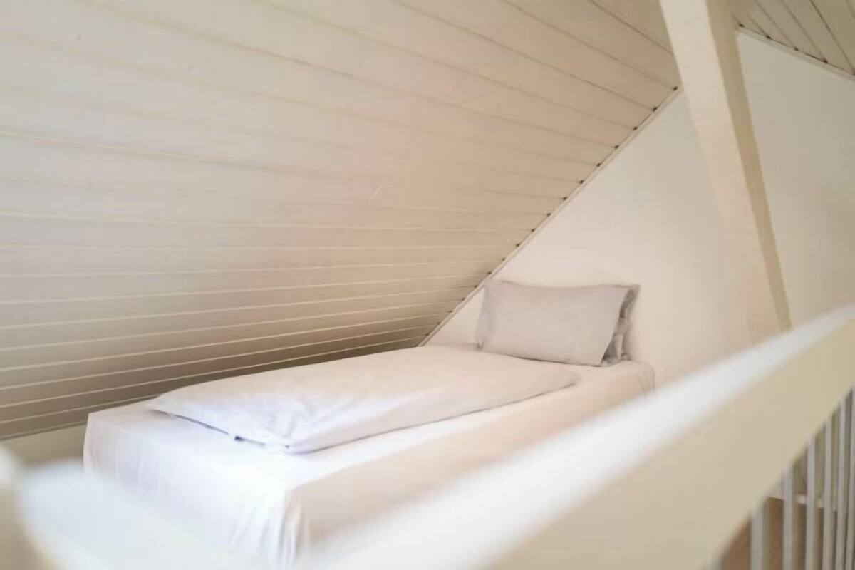 Une petite chambre avec un lit simple, un plafond en pente et une rambarde blanche.