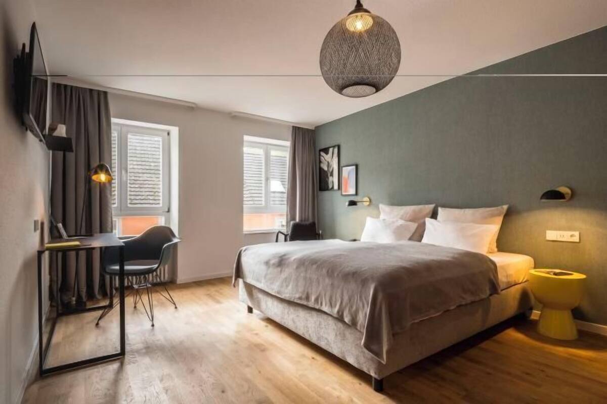 Une chambre à coucher comprenant un lit, un bureau, une chaise, un luminaire suspendu et une fenêtre.