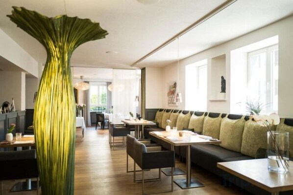 A modern dining area with a long table, chairs, and a large green vase centerpiece. - Genusshotel Krone & Roadtrips bei Basel (Inzlingen)