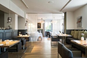 A modern dining area with high tables and chairs, a bar area with stools, and a view of the outdoors through a glass door. - Genusshotel Krone & Roadtrips bei Basel (Inzlingen)