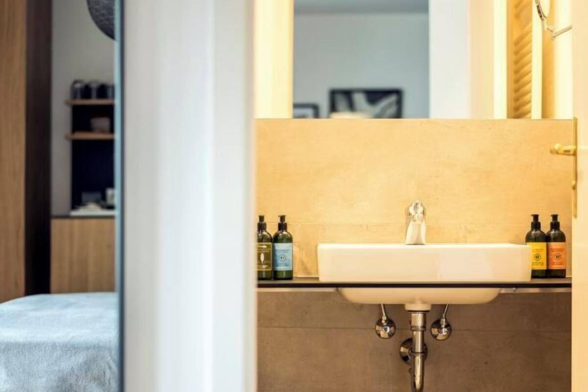 Une salle de bain avec un lavabo blanc, deux flacons de produits de toilette posés sur le comptoir et un miroir au-dessus du lavabo.