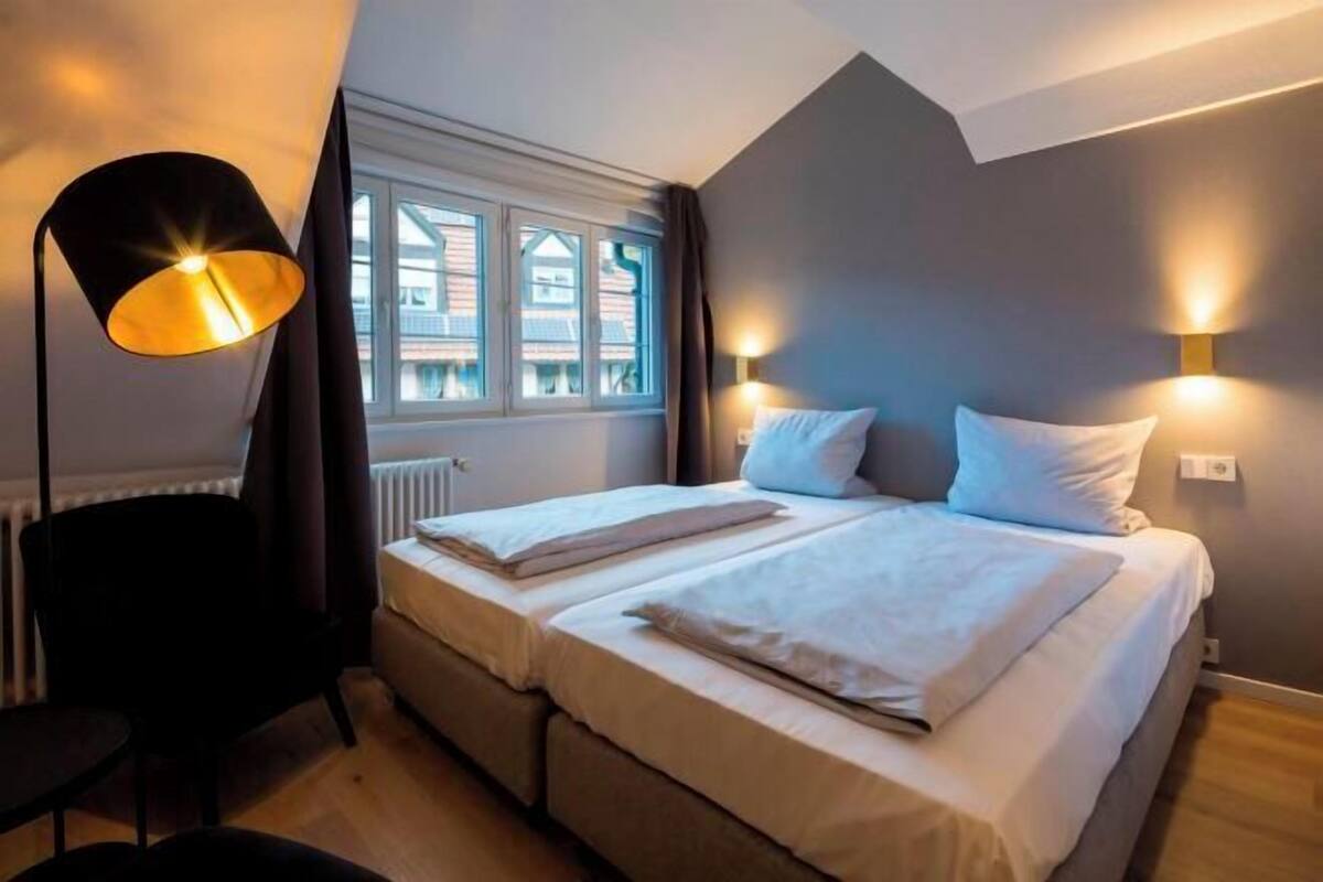 Une chambre à coucher avec un lit, deux tables de chevet, une chaise, une fenêtre et une lampe.