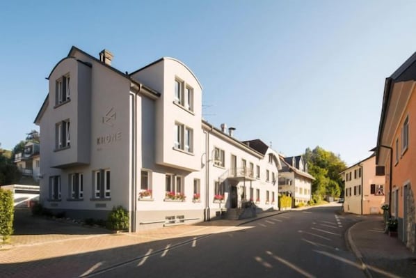 A two-story building with a flat facade, a visible entrance, and a clear sky. - Genusshotel Krone & Roadtrips bei Basel (Inzlingen)