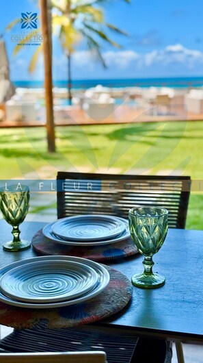 A table set with plates and a glass, overlooking a beach and palm trees.