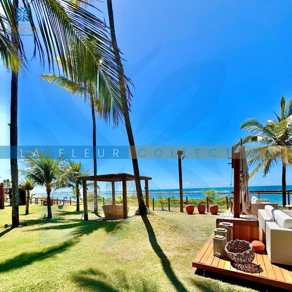 Un patio frente a la playa con muebles de madera, una hamaca y vista al océano.