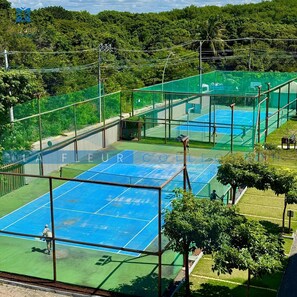 Una cancha de tenis con red, rodeada por una cerca verde y árboles.