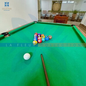 A pool table with a white cue ball and numbered balls, a green felt surface, and a visible logo 'LA FLEUR COLLECTION' on the table.