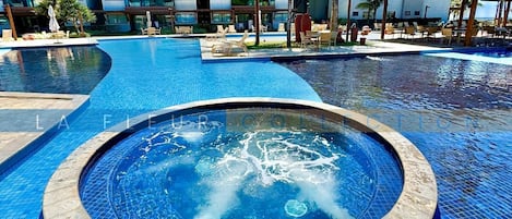 Une piscine avec un jacuzzi au centre, entourée de chaises longues et de palmiers.