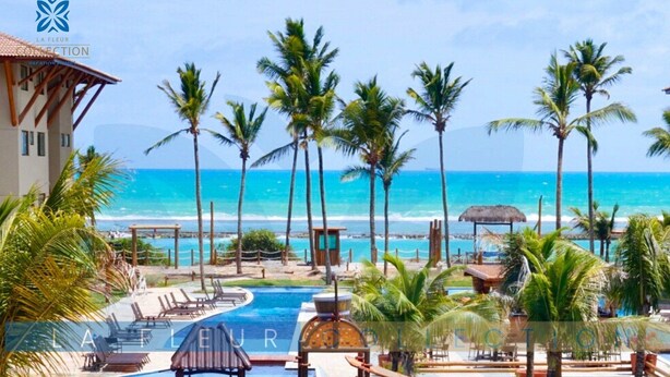 A resort pool area with a slide, lounge chairs, and palm trees. - Luxury Pool View at La Fleur Polynesia (Porto de Galinhas)