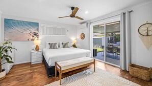A bedroom with a bed, bedside tables, a ceiling fan, a large window, and a view of the outdoors. - Family-friendly Home With Private Pool and BBQ (Sunshine Coast)