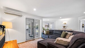 A modern living room with a dark grey sofa, a wooden coffee table, and a large window. - Family-friendly Home With Private Pool and BBQ (Sunshine Coast)