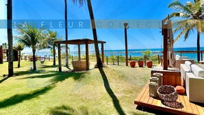 A beachside patio with wooden furniture, a hammock, and a view of the ocean. - Luxury Sea Front Foot on the Sand at La Fleur Polynesia (Porto de Galinhas)