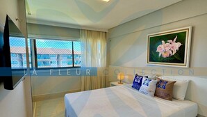 A hotel room with a bed, a TV mounted on the wall, a window with curtains, and a painting on the wall.