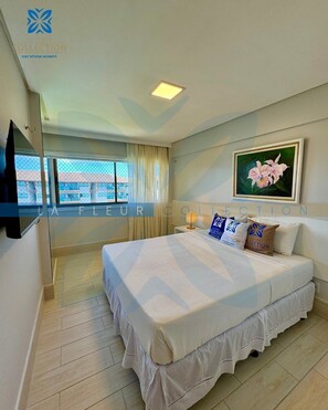 Habitación de hotel con cama, televisor montado en la pared, ventana con cortinas y un cuadro en la pared.
