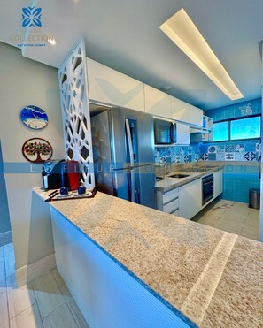 A modern kitchen with a granite countertop, stainless steel appliances, and blue-tiled backsplash.