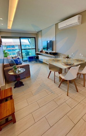 A modern living room with a sofa, a dining table set for four, and a TV mounted on the wall.
