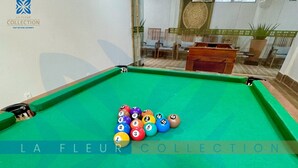 Uma mesa de bilhar com bola branca e bolas numeradas, superfície de feltro verde e o logo 'LA FLEUR COLLECTION' visível na mesa.