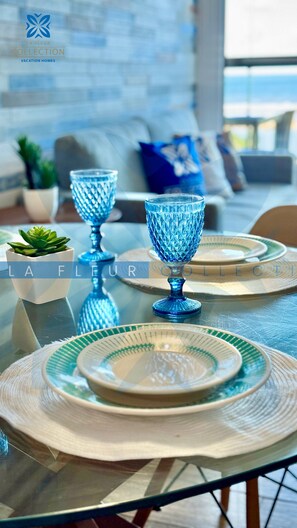 Een eettafel met blauw glaswerk, groene borden en geweven placematen.