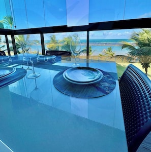 Un coin repas avec une table en verre, des chaises et une vue sur la plage.