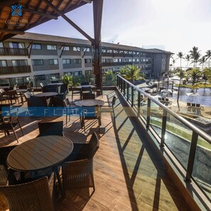 Varanda de hotel com área de estar externa, piscina e vista dos edifícios ao redor.