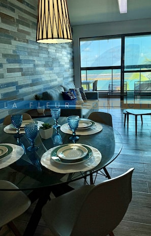 Un espace de restauration moderne avec une table en verre, de la verrerie bleue et une vue sur l’océan grâce à de grandes fenêtres.