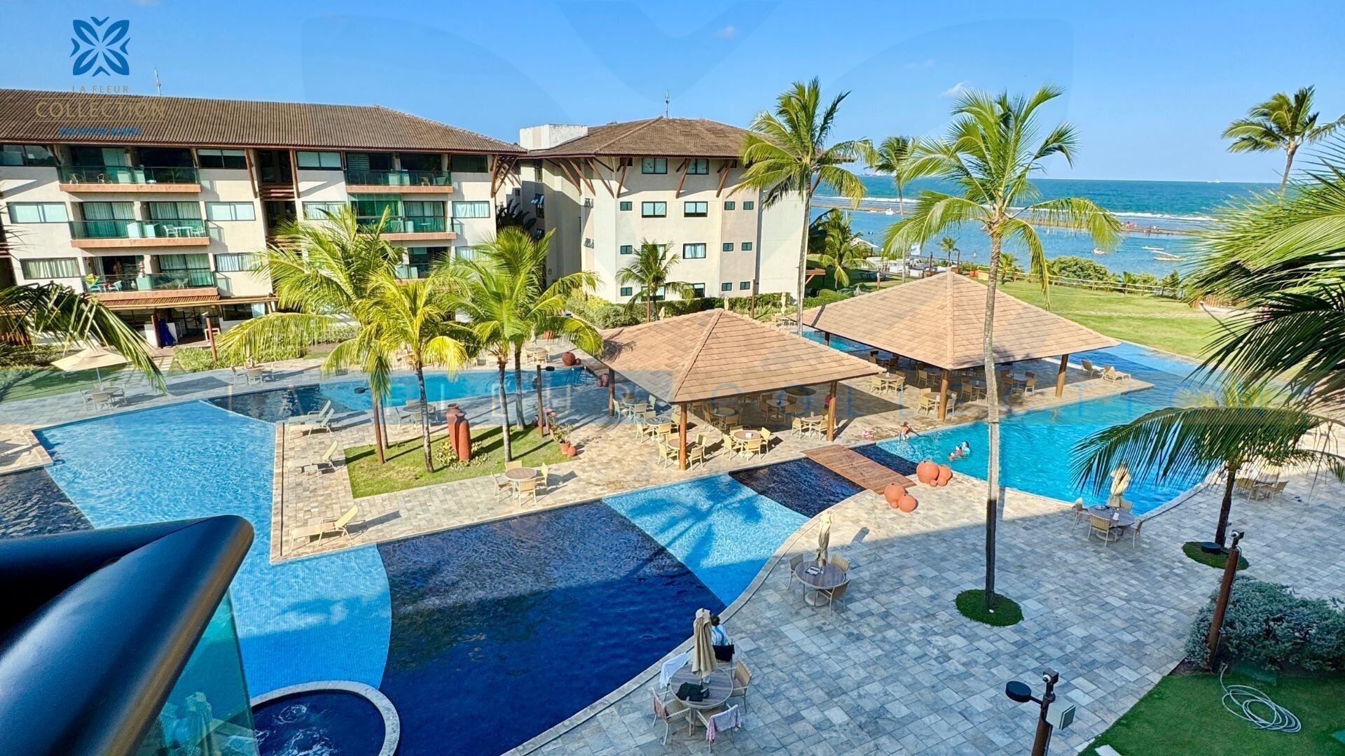 A hotel with a pool area, palm trees, and a view of the ocean.