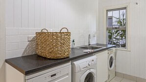 Un espace buanderie comprenant un lave-linge, un évier et une fenêtre donnant sur un paysage verdoyant.