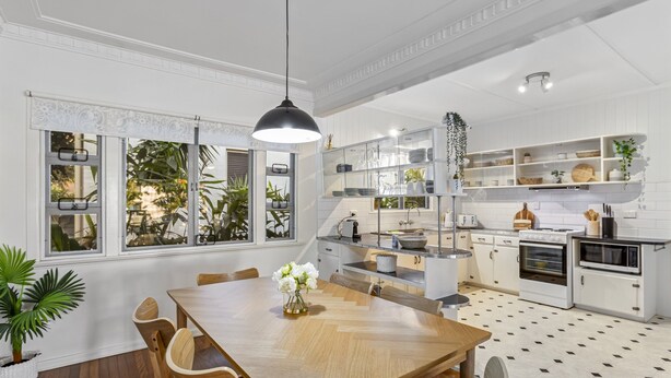 Une cuisine moderne avec des meubles blancs, une table à manger en bois et un luminaire suspendu noir.