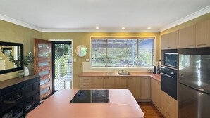 A modern kitchen with a central island, stainless steel appliances, and a window with blinds. - Pet-friendly 2-bed Beach House With Garden & BBQ (Surf Beach)