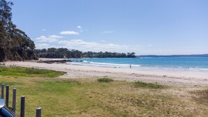 A beach with a sandy shore, a grassy foreground, and a forested area in the background. - Pet-friendly 2-bed Beach House With Garden & BBQ (Surf Beach)