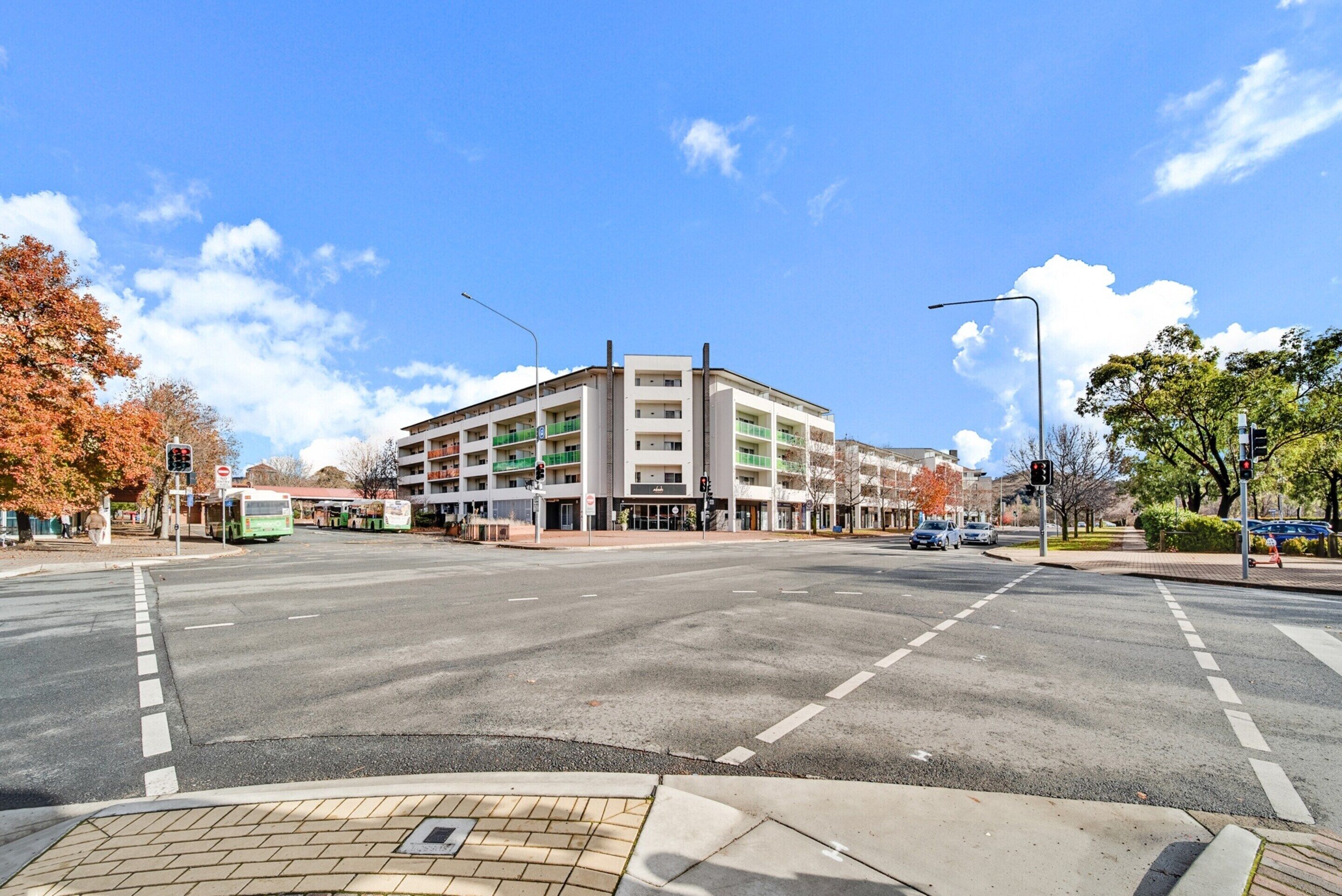 A multi-story building with a central entrance, surrounded by a crosswalk and traffic lights.