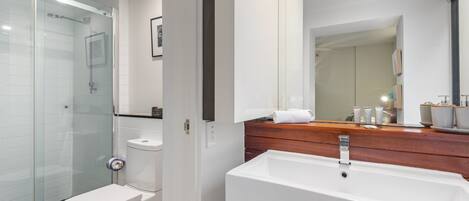 A modern bathroom with a glass shower enclosure, a white toilet, a wooden vanity with a sink, and a large mirror.