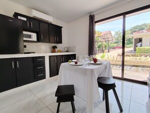 A modern kitchen with black cabinets, a white countertop, and a dining table set for two. - Studio Apartment, Pool, Kitchen, A/C, Playa Grande, Guanacaste, close to beaches (Matapalo)
