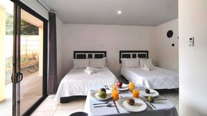 Habitación de hotel con dos camas, una mesa de comedor con desayuno y una puerta corrediza de vidrio al exterior.