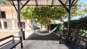 Un espacio al aire libre techado con una hamaca, bancos y suelo de grava.