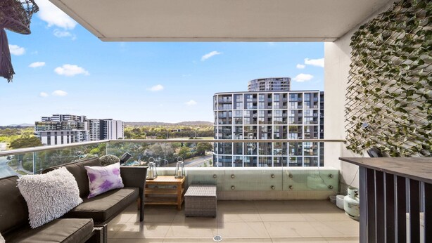 A balcony with a sofa, cushions, a small table, and a potted plant. - Elegant 2-bed With Pool, Alfresco Dining & Balcony (Canberra)