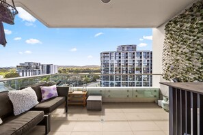 A balcony with a sofa, cushions, a small table, and a potted plant. - Elegant 2-bed With Pool, Alfresco Dining & Balcony (Canberra)