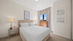 A neatly arranged hotel room with a large bed, bedside lamps, a dresser, and framed artwork on the walls. - Elegant 2-bed With Pool, Alfresco Dining & Balcony (Canberra)