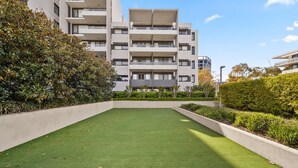 A modern apartment building with multiple balconies, a well-maintained lawn, and surrounding greenery. - Elegant 2-bed With Pool, Alfresco Dining & Balcony (Canberra)
