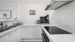 A modern kitchen with white cabinetry, a stainless steel sink, a microwave, and a black induction cooktop. - Stylish 1-bed Stay With Balcony & Study (Canberra)