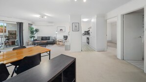 A spacious living area with a wooden dining table, a sofa, and a kitchen in the background. - Stylish 1-bed Stay With Balcony & Study (Canberra)