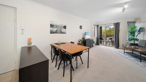 A dining area with a wooden table and black chairs, a dark cabinet, a clock, and a painting on the wall. - Stylish 1-bed Stay With Balcony & Study (Canberra)