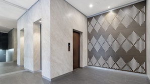 A modern hallway with a patterned wall, a door, and a light fixture. - Stylish 1-bed Apartment With Rooftop Access (Perth)