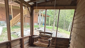 A wooden deck with a bench and a table, large windows, and a view of a forested area.