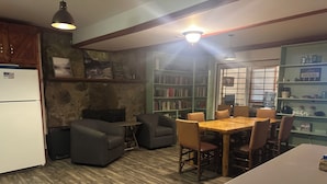 A cozy kitchen with a dining area, wooden cabinets, a refrigerator, and a bookshelf filled with books.