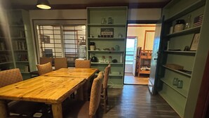 A dining area with a wooden table and chairs, surrounded by bookshelves and a kitchen area.