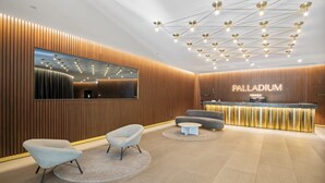 A modern reception area with a wooden panel wall, a large mirror, a reception desk, and a seating area with two armchairs and a round table. - Stylish 2-bed Apartment With Stunning City Views (Melbourne)