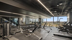 A modern gym with various exercise equipment, large windows, and a city view. - Stylish 2-bed Apartment With Stunning City Views (Melbourne)