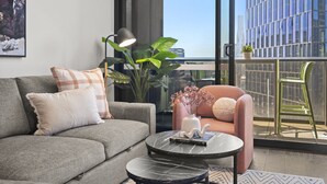 A modern living room with a grey sofa, a pink armchair, a round black coffee table, and a large window with a city view. - Stylish 2-bed Apartment With Stunning City Views (Melbourne)