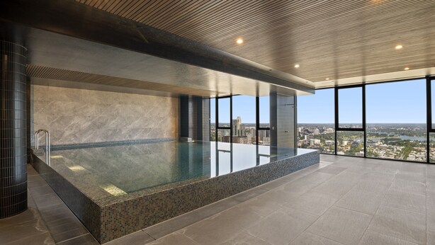 A modern indoor pool with a city view, featuring a large rectangular pool, a tiled floor, and a ceiling with linear lighting. - Stylish 2-bed Apartment With Stunning City Views (Melbourne)